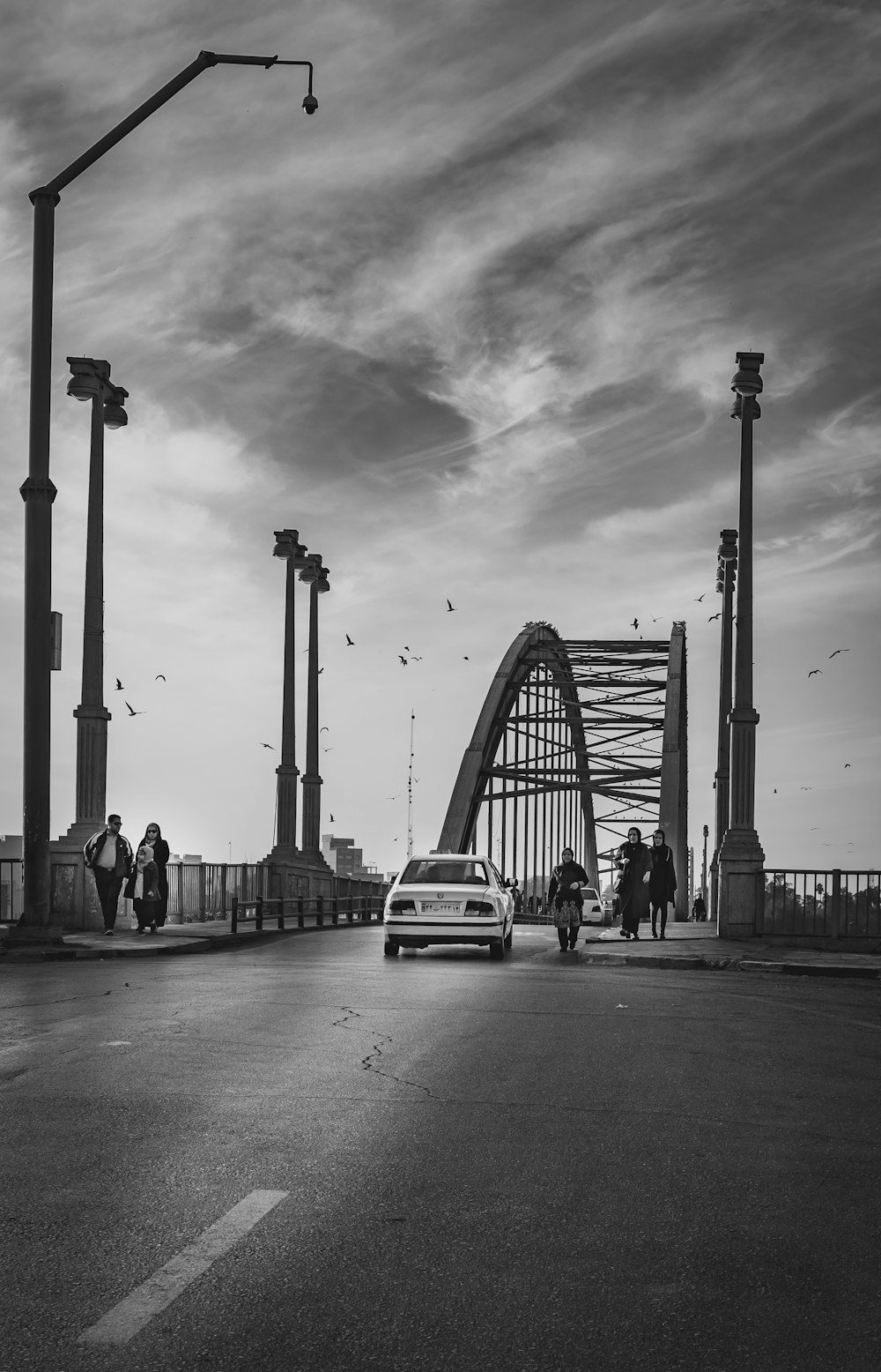 Photographie en niveaux de gris d’un pont avec un véhicule et des personnes marchant