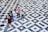 Several people stand on a geometric tiled floor featuring a black and white pattern of squares and diamonds. Some appear to be engaged in conversation while others are using their phones. The wet patches on the tiles suggest recent rain.
