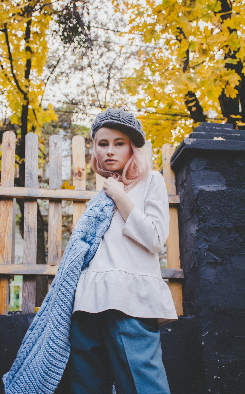 woman in white long-sleeved shirt stands beside black post and wooden fence