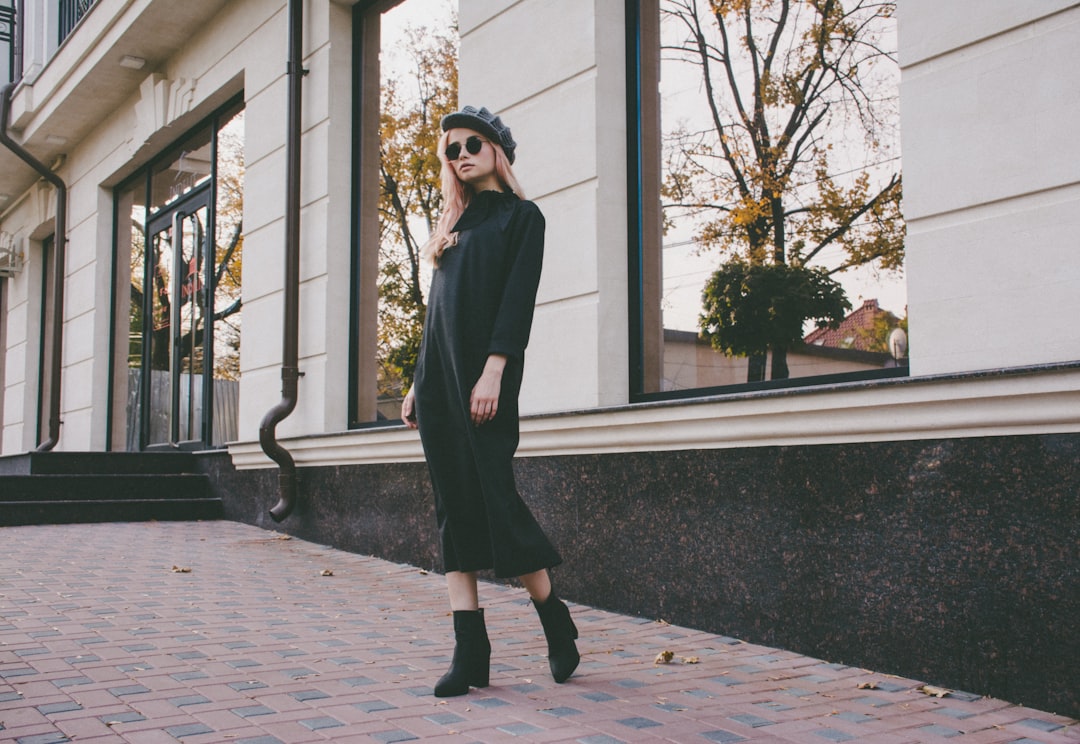 selective focus photography of standing woman wearing gray flat cap and black long-sleeved dress during daytime