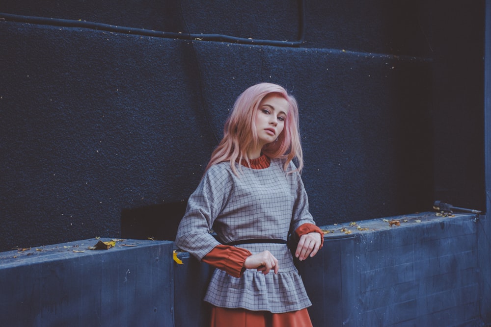 woman in grey windowpane checked shirt leans on grey concrete wall