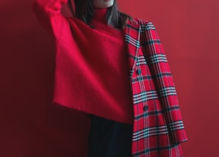 woman holding her head wearing red long-sleeved shirt and half of coat