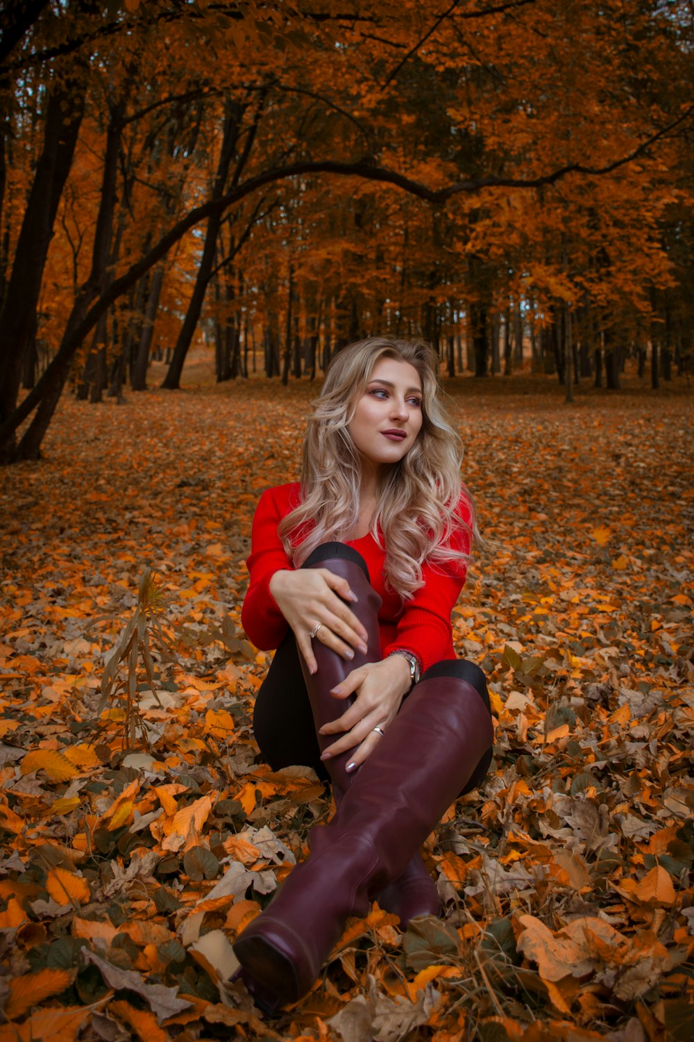 woman in red sweater sits on ground covered with leaves