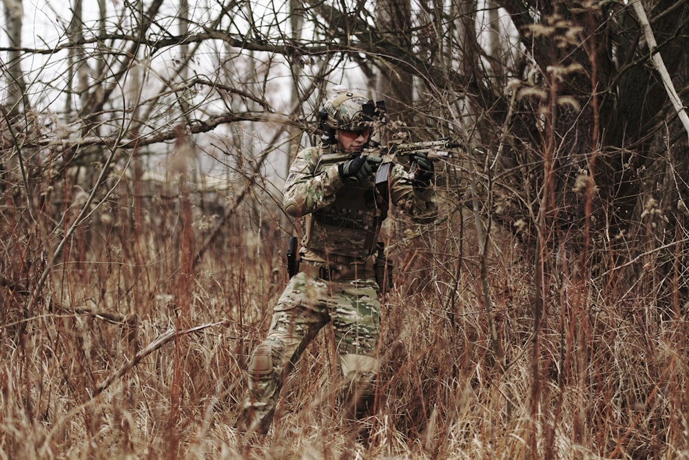 man holding assault riffle beside bare tree