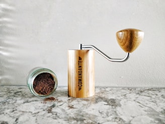 Compact black manual coffee grinder resting on a kitchen counter next to a steaming cup of coffee.