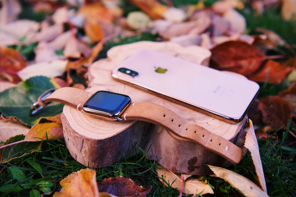 silver iPhone X beside gold aluminum case Apple Watch with leather strap on wood slice