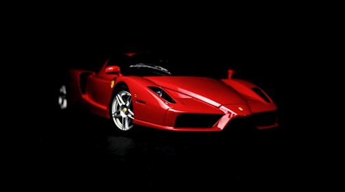 A sleek, red sports car with a shiny finish is prominently displayed against a black background. The car's aerodynamic design and polished surface highlight its luxury and performance features.