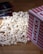 A pile of popcorn spilled out from a red and white striped container, with several DVD cases laying nearby on a wooden surface.