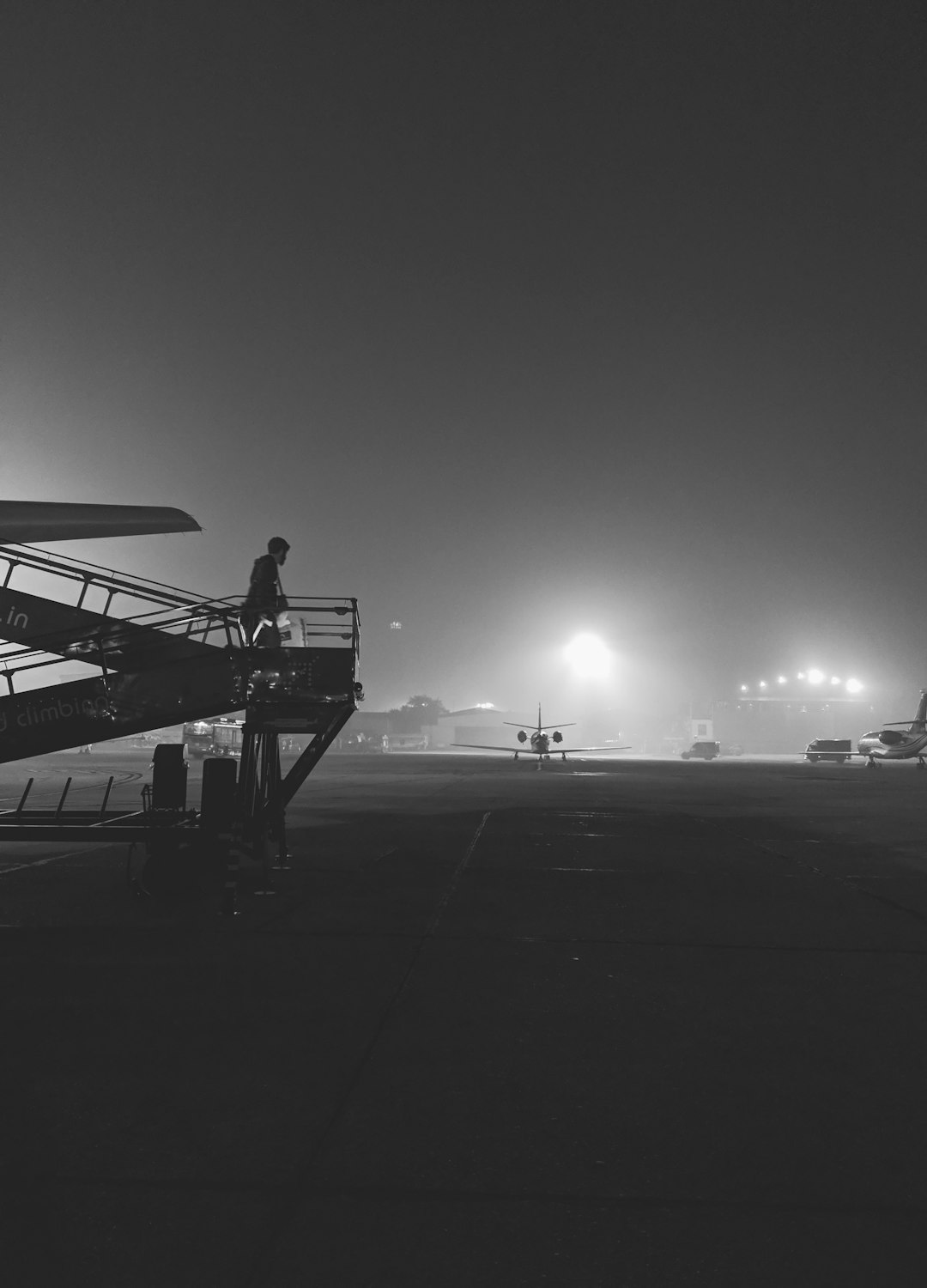 grayscale photography of person walking on airliner stairs