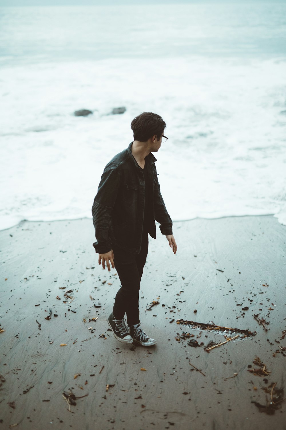 man wearing black jacket and denim jeans on seashore