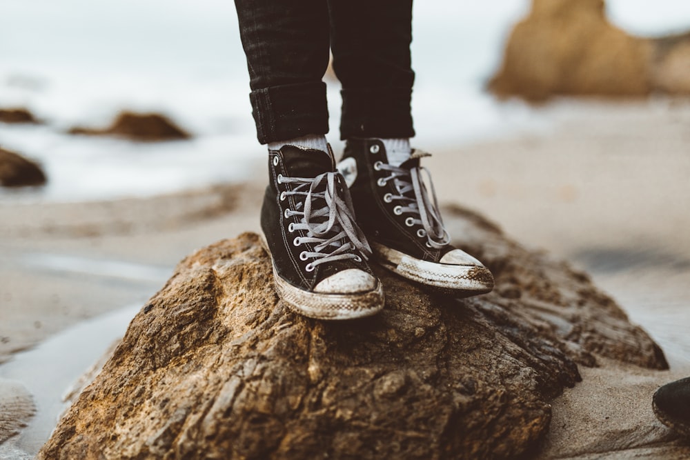 person wearing sneakers standing on rock at the shore