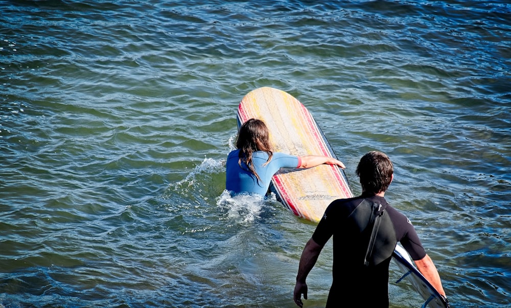 woman holding surfboard near man standing on body of water