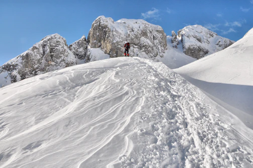 Snow-capped mountains under a bright blue sky, with a lone hiker admiring the view.