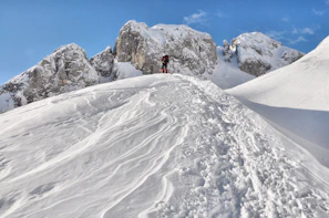Snow-capped peaks towering under a clear blue sky with a lone hiker in the foreground.