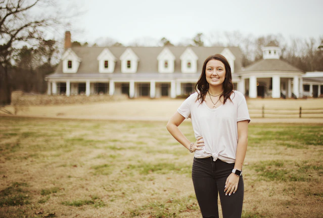 Erica Shakoor confidently standing in front of a stunning luxury Atlanta home at sunset.