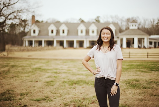 A friendly realtor standing outside a charming house, smiling and ready to assist clients.