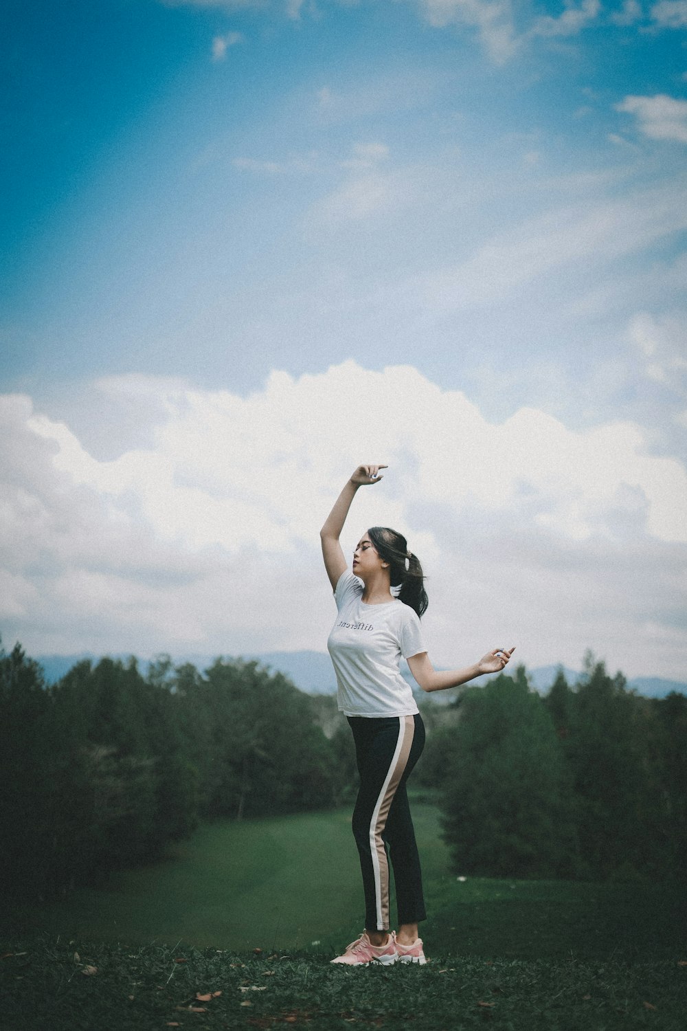 woman in white shirt standing on grass field under blue sky and white clouds during daytime