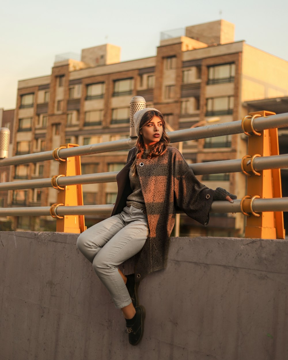 woman sitting on grey concrete fence during daytime