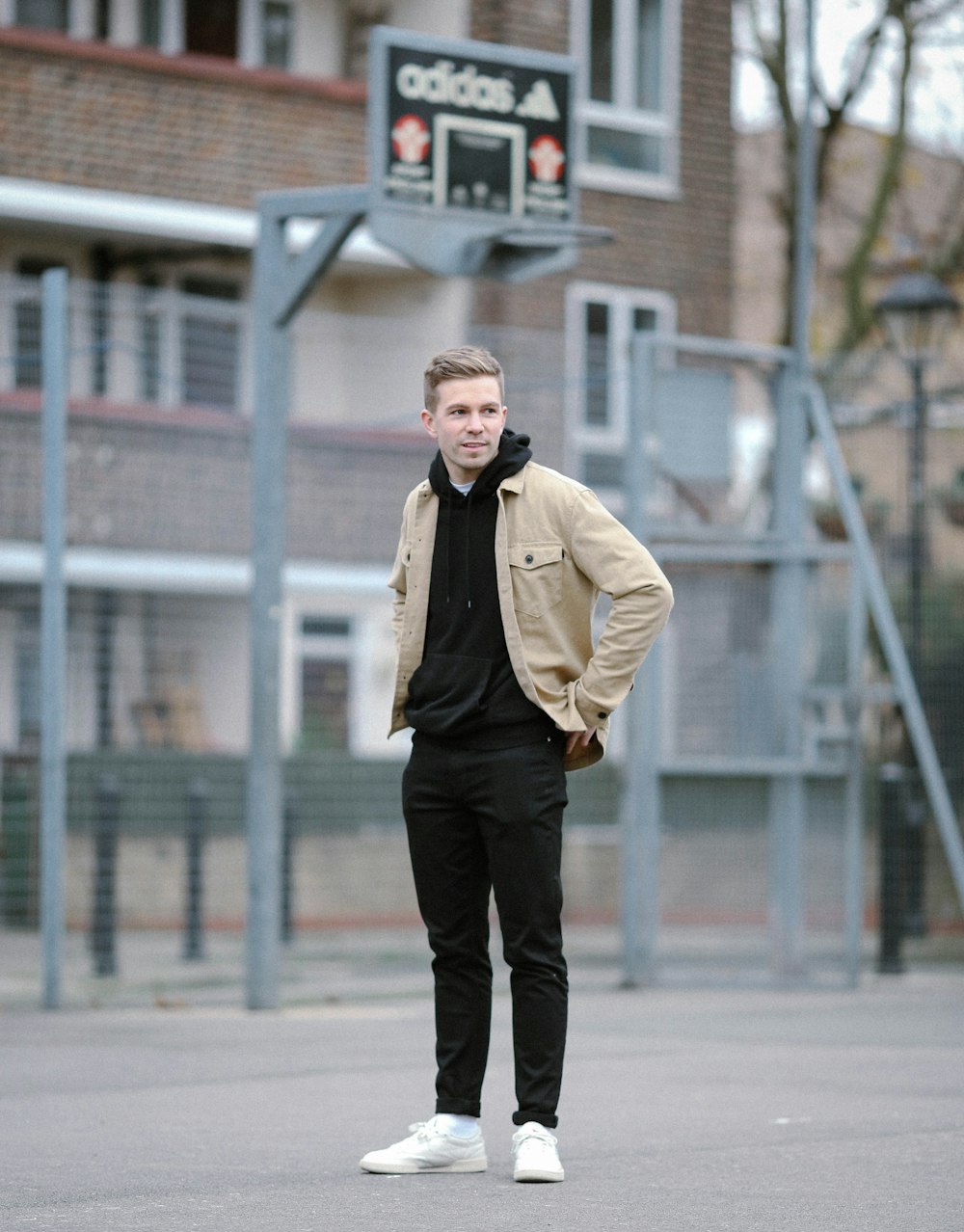 man wearing brown jacket and black pants standing near basketball ring