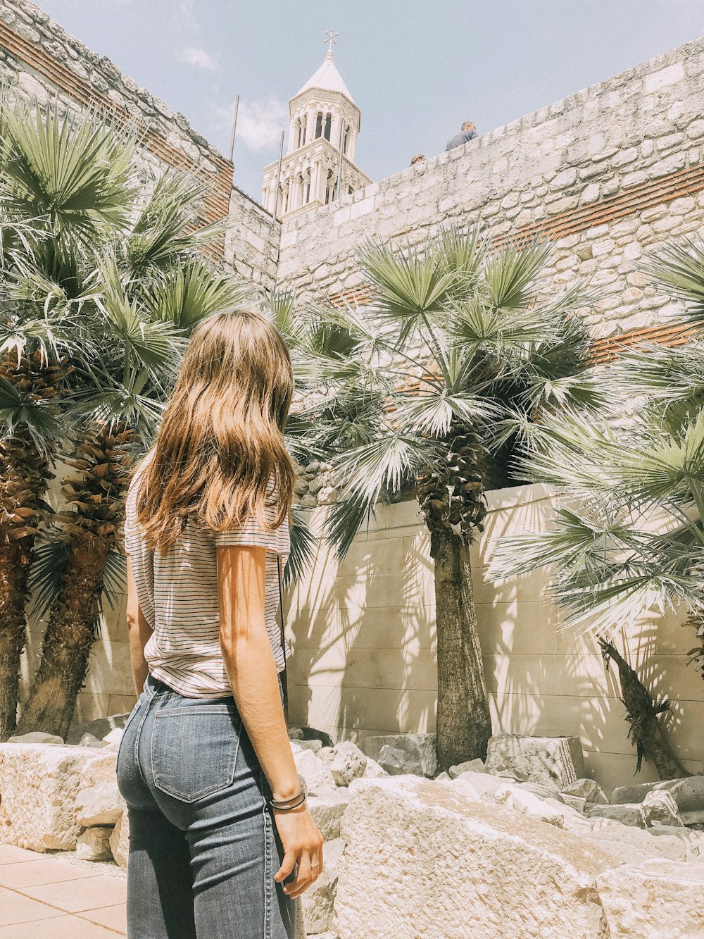 Femme debout près des palmiers et du mur de béton pendant la journée