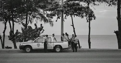 A group of veterans in blue uniforms gathered around a Volvo VNL 860 metallic blue truck on the enclosed driving track.