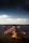 A breathtaking view of the Grand Canyon under a starry night sky, with dramatic shadows cast across the layered rock formations in varying hues of red, orange, and brown. The landscape has a serene and majestic atmosphere with clouds scattered across the horizon.