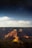 A breathtaking view of the Grand Canyon under a starry night sky, with dramatic shadows cast across the layered rock formations in varying hues of red, orange, and brown. The landscape has a serene and majestic atmosphere with clouds scattered across the horizon.