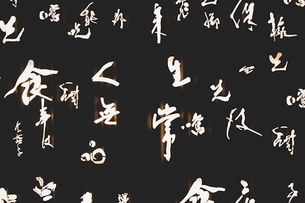 Bright and elegant calligraphy characters in a script-like style are illuminated against a dark background, creating a striking contrast.