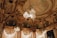 An opulent interior with intricate architectural detailing adorned with gold elements. Crystal chandeliers hang from the ceiling, casting a warm glow. The ceiling features elaborate frescoes and decorative moldings. The room exudes luxury and grandeur.