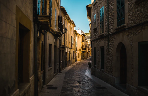 An old European village street lined with stone buildings and cobblestones under a soft afternoon light.