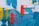 An abstract painting features bold and vivid brushstrokes. Shades of blue create a textured background, overlaid with vibrant red vertical patterns resembling wire or grid structures. Yellow streaks add contrast and dynamic energy to the composition.