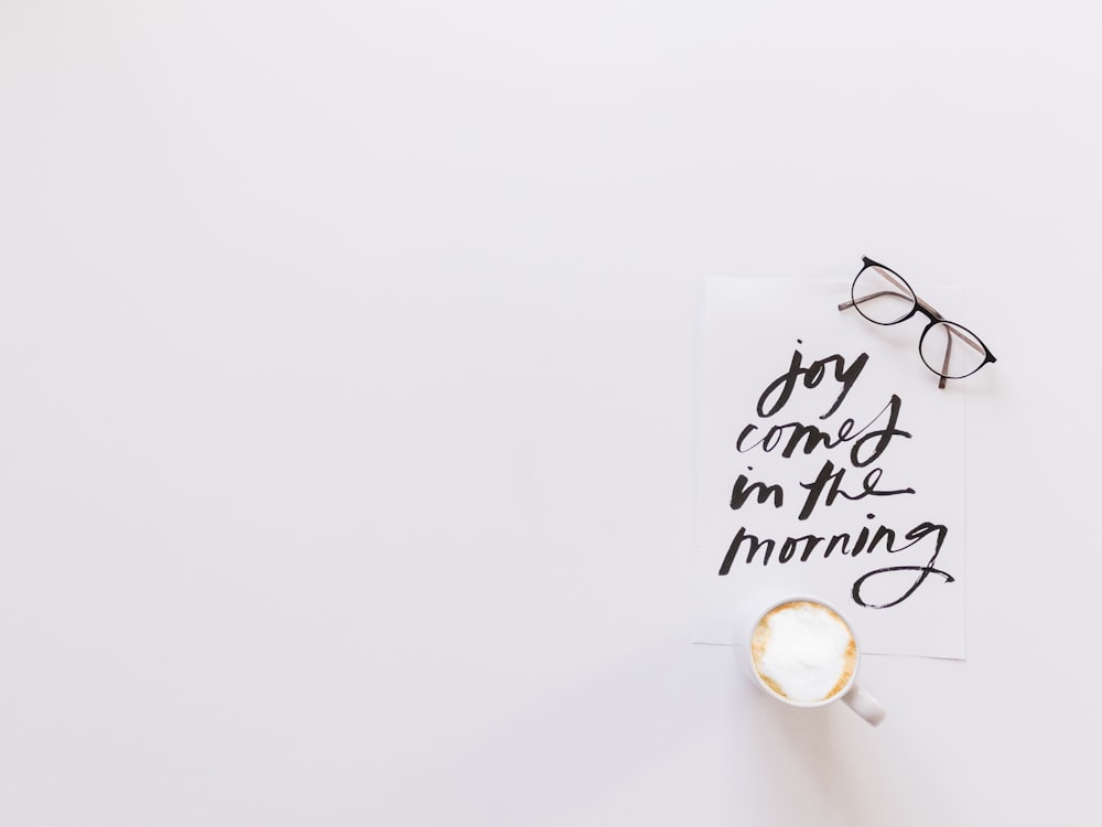 brown eyeglasses and latte on top of joy comes in the morning note