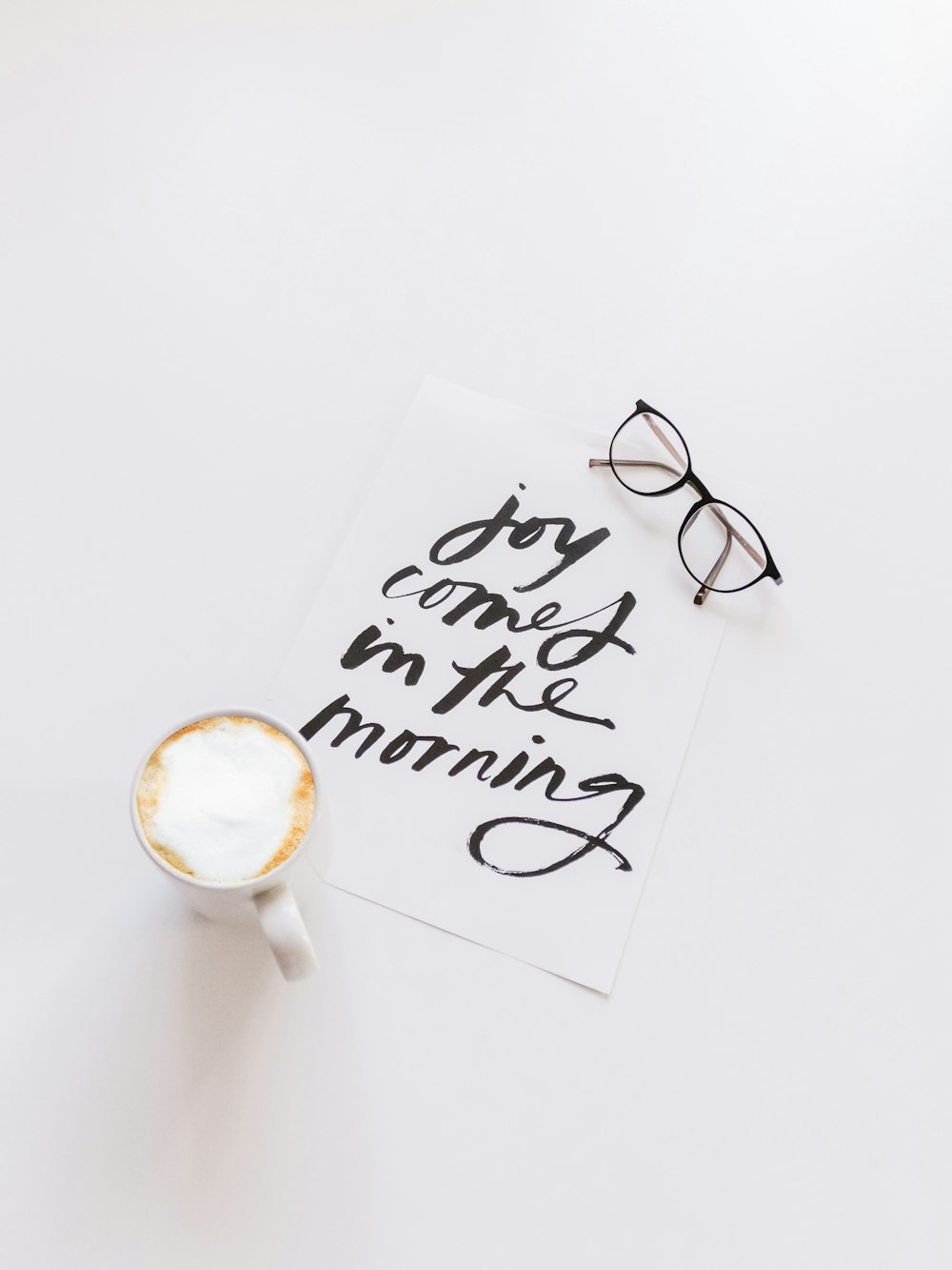 black framed eyeglasses beside white ceramic coffee cup