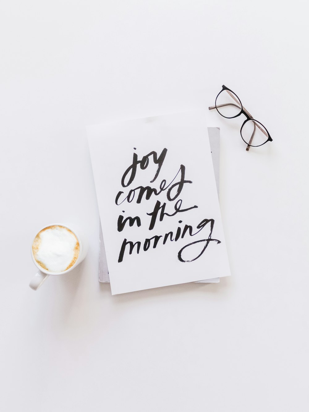 brown framed eyeglasses,latte, and joy comes in the morning note on white surface