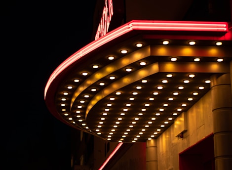 A brightly lit marquee with rows of illuminated bulbs, featuring red accents. The structure is set against a dark night sky, creating a striking contrast.