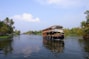 A serene backwater houseboat gliding through lush green Kerala canals at sunset