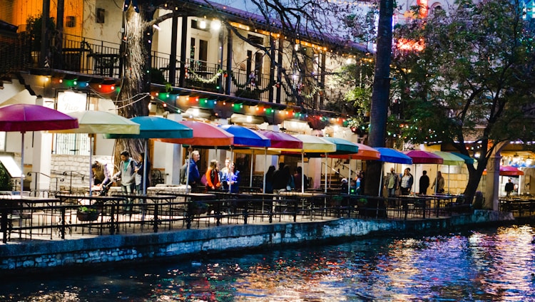 Outdoor riverside dining area with wooden tables and soft lighting at sunset.
