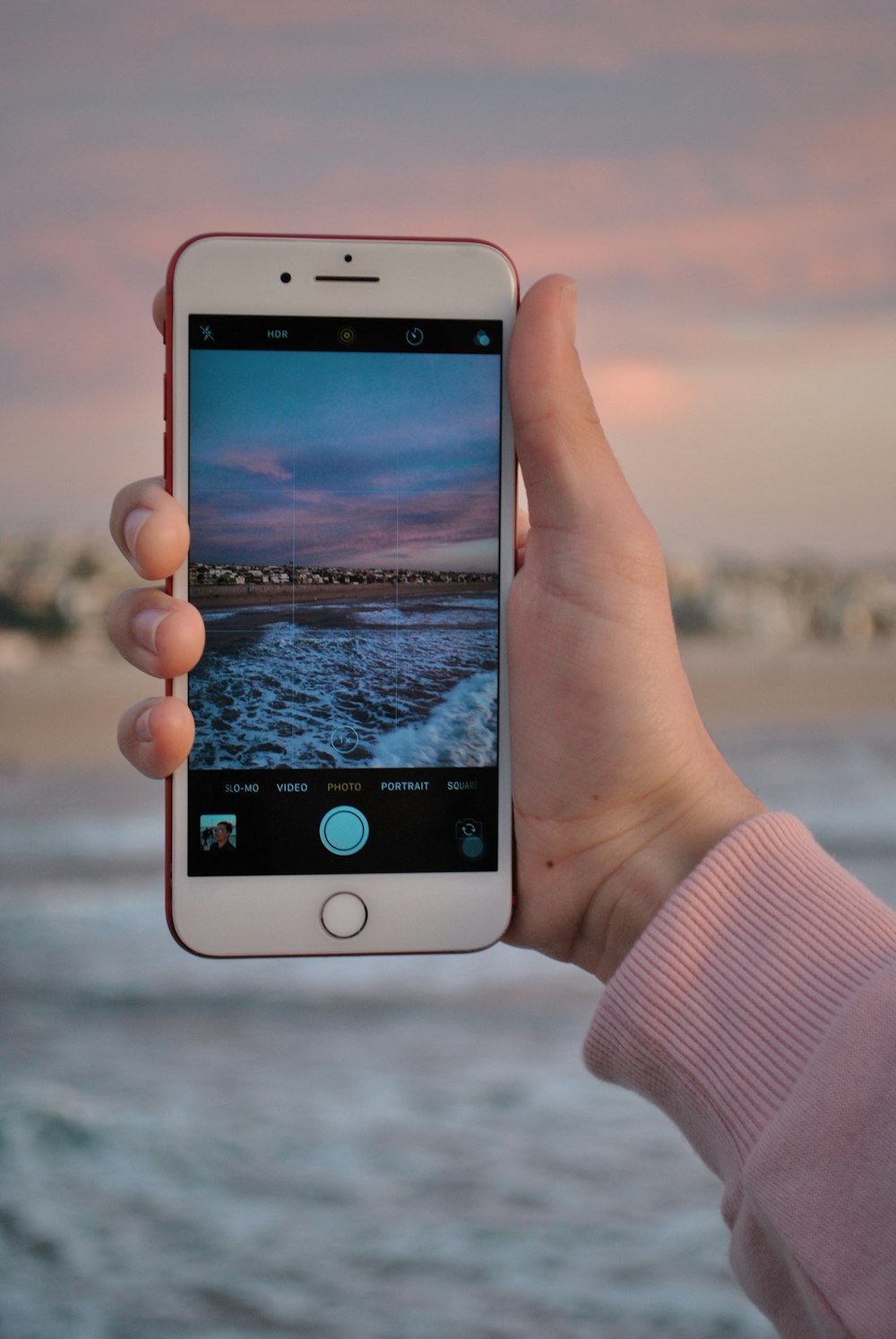 person using PRODUCT RED iPhone 7 with seashore wallpaper