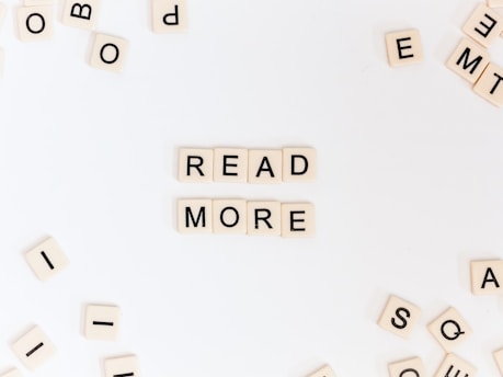 Scrabble tiles arranged to form the words 'READ MORE' are centered on a white background, with additional scattered tiles surrounding them.