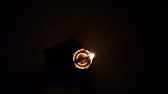 A single burning diya or candle is placed at the center, with a dark background enveloping the scene. The flame casts a warm, gentle glow, highlighting the circular shape of the vessel containing it.