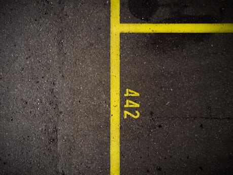 A dark asphalt surface is divided by bright yellow lines, with the number '442' marked beside the lines. The texture of the asphalt is rough and contains small pebbles and imperfections.