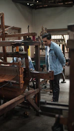 Close-up photo of students weaving silk threads on a traditional loom inside the museum workshop.