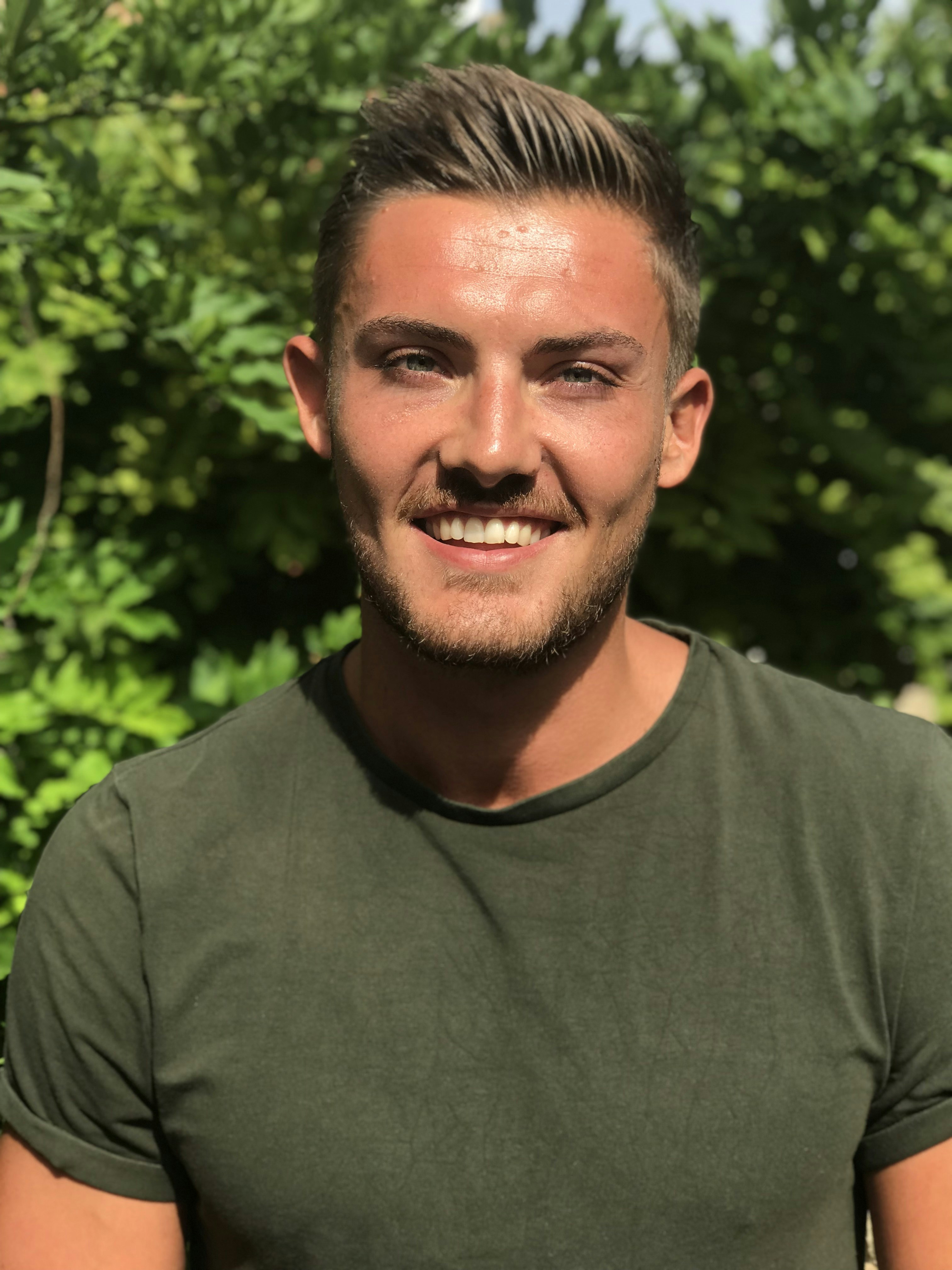 Friendly young man with warm smile in casual outdoor setting with green background