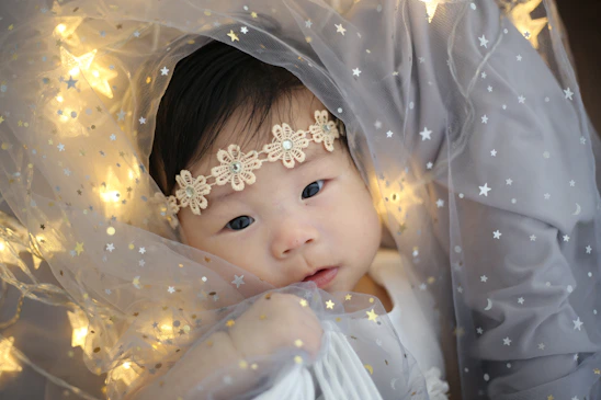 A softly lit photo of baby Riya Sanvi surrounded by pastel-colored stars and floating hearts.