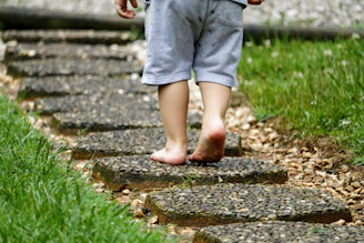 A candid shot of a child playing barefoot on a sandy path surrounded by greenery.