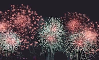 Bursting fireworks of various colors illuminate the night sky, with patterns spreading outward in vibrant hues. The scene captures the excitement and beauty of a celebratory event.