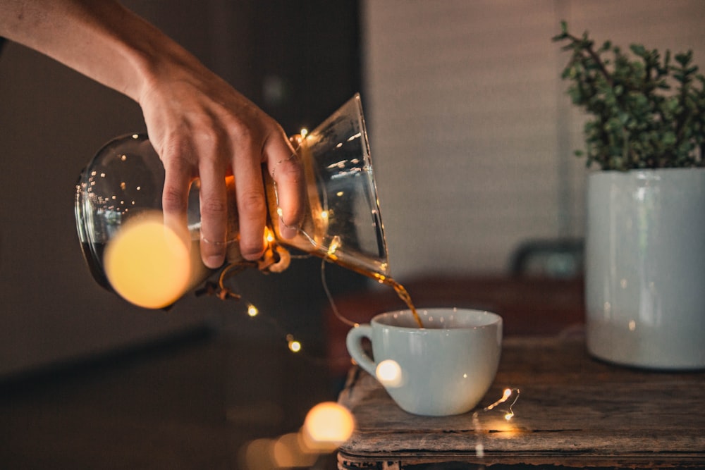 person pouring coffee on white teacup