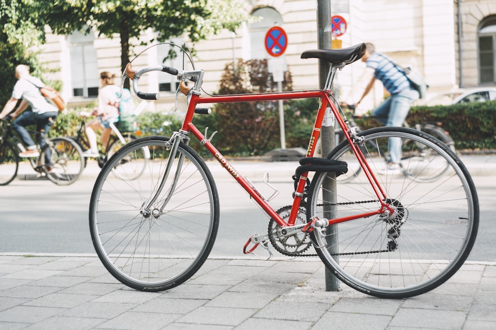 Bicicletta da strada rossa e nera appoggiata su palo in acciaio grigio