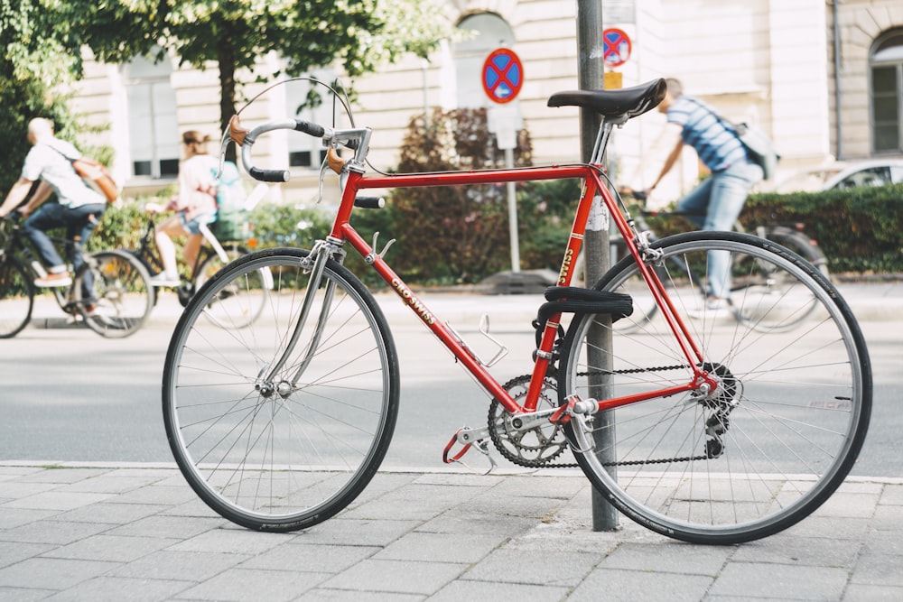 red and black road bicycle leaning on gray steel post