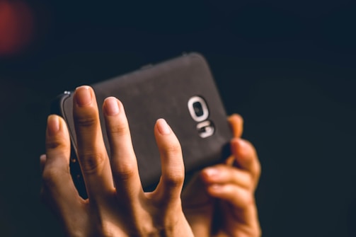 Hands holding a smartphone connected to a compact Bluetooth device.
